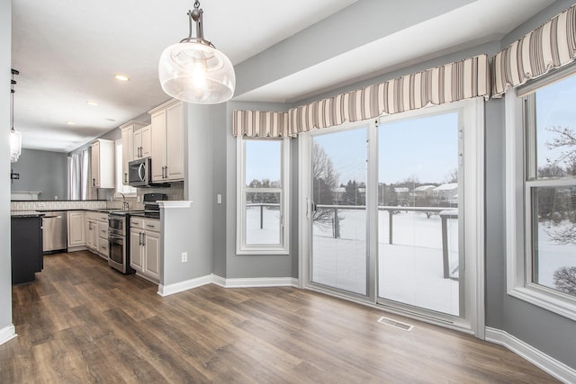 kitchen with appliances with stainless steel finishes, dark wood-type flooring, a sink, and baseboards