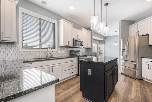 kitchen with pendant lighting, stainless steel appliances, white cabinets, a sink, and wood finished floors