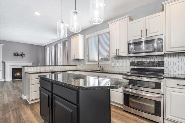 kitchen with decorative backsplash, a peninsula, a lit fireplace, stainless steel appliances, and a sink