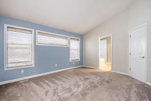 unfurnished bedroom featuring lofted ceiling, multiple windows, carpet flooring, and ensuite bathroom