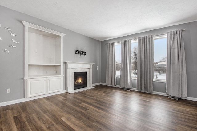 unfurnished living room with dark wood finished floors, a textured ceiling, and a tile fireplace