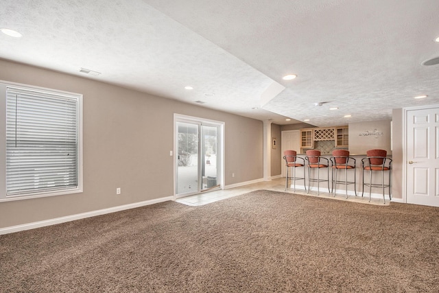 unfurnished living room featuring a textured ceiling, a bar, and carpet