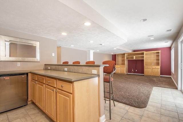 kitchen featuring a textured ceiling, dishwashing machine, light carpet, and a kitchen breakfast bar