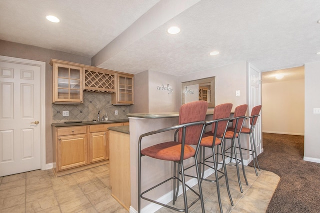 kitchen featuring tasteful backsplash, baseboards, dark countertops, glass insert cabinets, and a kitchen breakfast bar