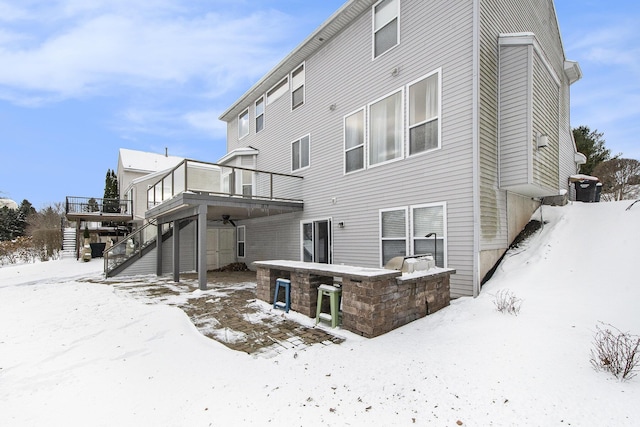 snow covered property with an outdoor kitchen, a wooden deck, and stairs