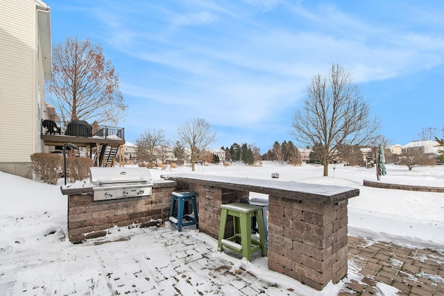 snow covered patio with outdoor dry bar, area for grilling, an outdoor kitchen, a wooden deck, and stairs