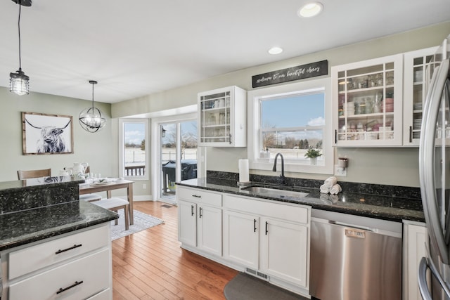 kitchen with white cabinetry, stainless steel appliances, dark stone counters, hanging light fixtures, and sink