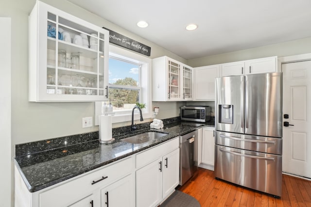 kitchen with dark stone countertops, sink, appliances with stainless steel finishes, white cabinets, and dark hardwood / wood-style flooring