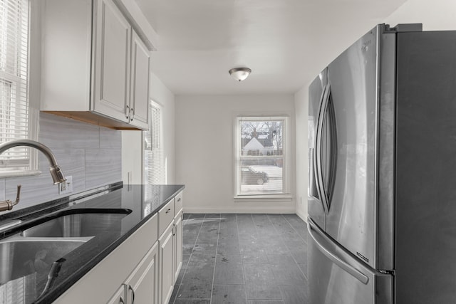 kitchen featuring white cabinets, stainless steel refrigerator with ice dispenser, dark stone counters, decorative backsplash, and sink