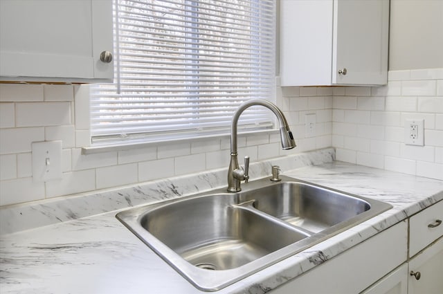 interior details with tasteful backsplash, white cabinets, light stone countertops, and sink