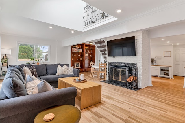 living room with built in shelves, ornamental molding, a fireplace, and light wood-type flooring