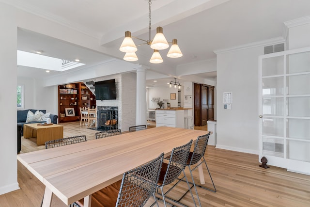 dining room with an inviting chandelier, crown molding, a fireplace, and light hardwood / wood-style floors