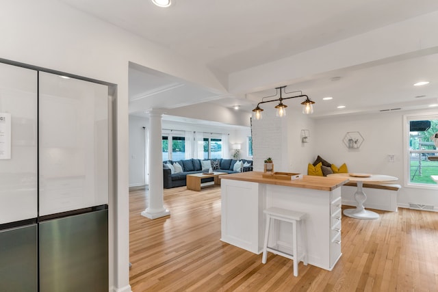 kitchen with light hardwood / wood-style flooring, decorative columns, white cabinets, a kitchen bar, and wood counters