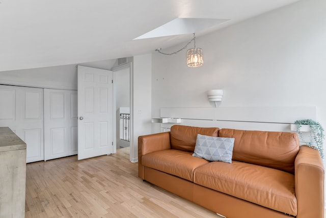 living room with vaulted ceiling with skylight, a notable chandelier, and light hardwood / wood-style floors