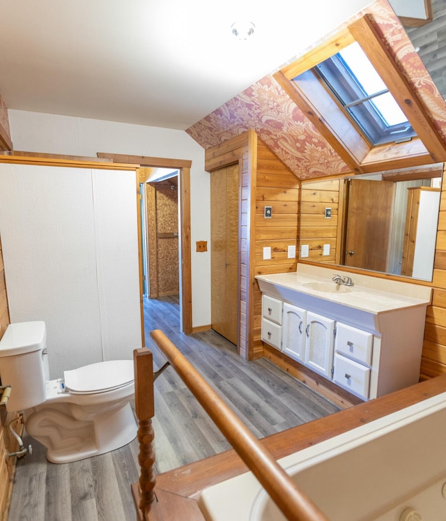 bathroom with toilet, vanity, lofted ceiling with skylight, wood walls, and wood-type flooring