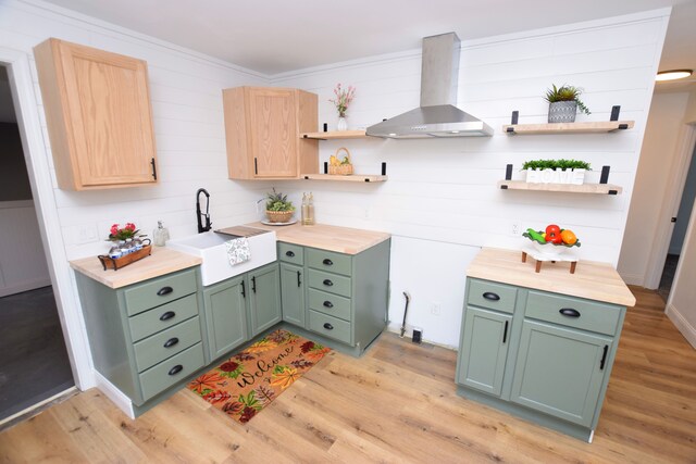 kitchen featuring wall chimney range hood, green cabinets, sink, and light brown cabinets