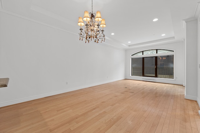 empty room featuring crown molding, an inviting chandelier, a tray ceiling, and light hardwood / wood-style flooring