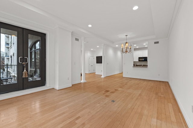 unfurnished living room featuring light hardwood / wood-style floors, a chandelier, a raised ceiling, and french doors