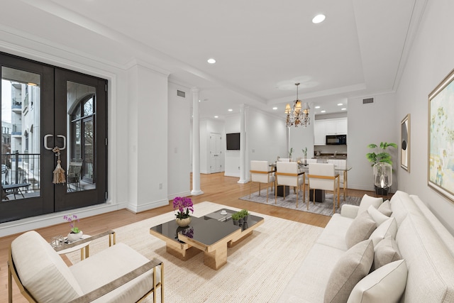 living room with a raised ceiling, light wood-type flooring, french doors, and a chandelier