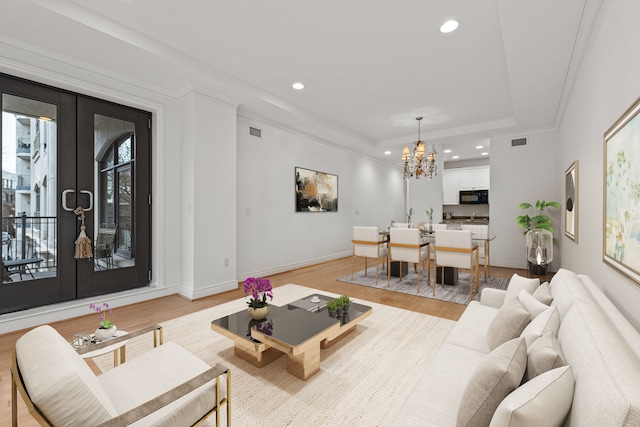 living room featuring french doors, a chandelier, a raised ceiling, and light wood-type flooring