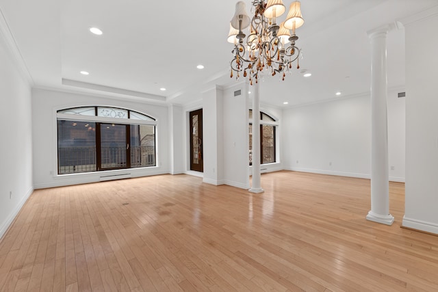 unfurnished living room with an inviting chandelier, light hardwood / wood-style floors, a raised ceiling, and decorative columns