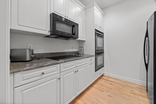 kitchen featuring black appliances, dark stone countertops, white cabinetry, and light hardwood / wood-style flooring