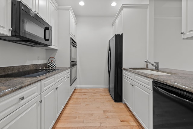 kitchen with black appliances, white cabinetry, dark stone counters, light hardwood / wood-style floors, and sink