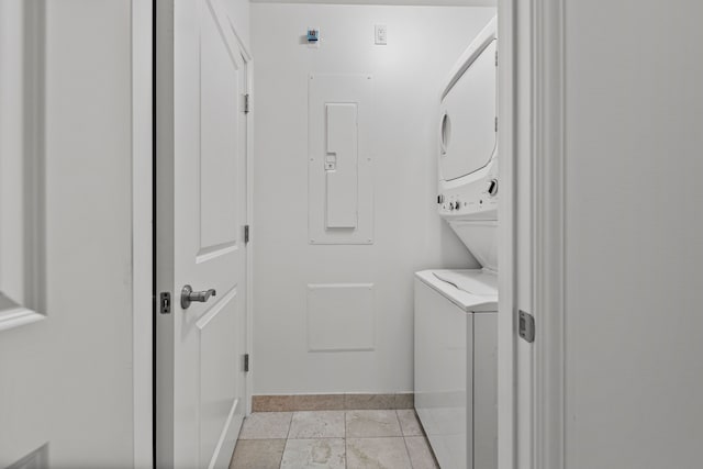 clothes washing area featuring stacked washer / dryer, light tile patterned flooring, and electric panel