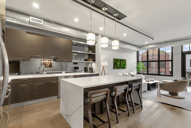 kitchen with dark brown cabinetry, dishwasher, a kitchen island, light hardwood / wood-style floors, and sink