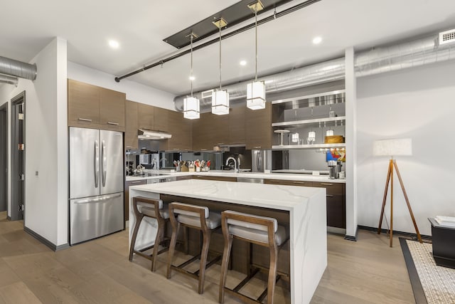 kitchen with a center island, sink, dark brown cabinetry, decorative light fixtures, and stainless steel fridge