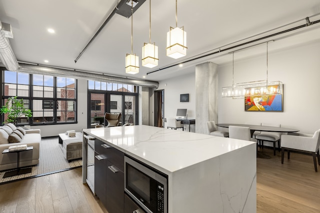 kitchen featuring decorative light fixtures, light hardwood / wood-style floors, stainless steel microwave, and a kitchen island