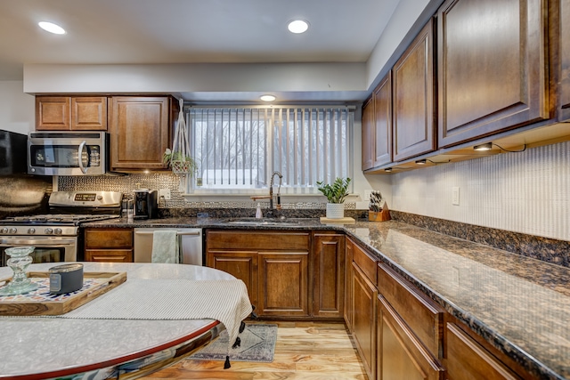 kitchen with dark stone countertops, sink, appliances with stainless steel finishes, and light wood-type flooring