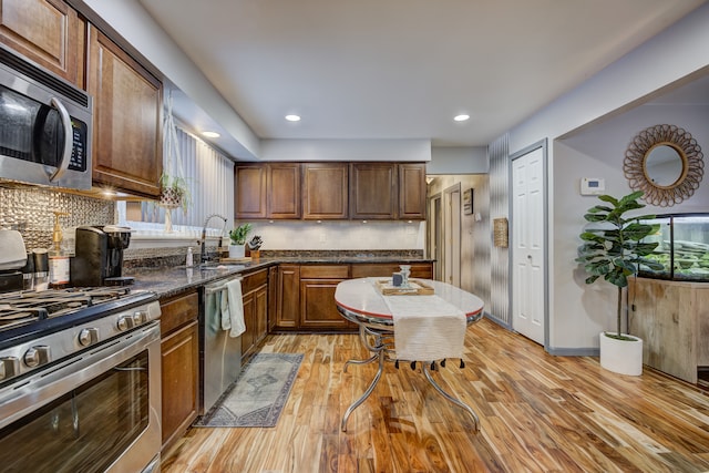 kitchen with stainless steel appliances, dark stone countertops, tasteful backsplash, sink, and light hardwood / wood-style flooring