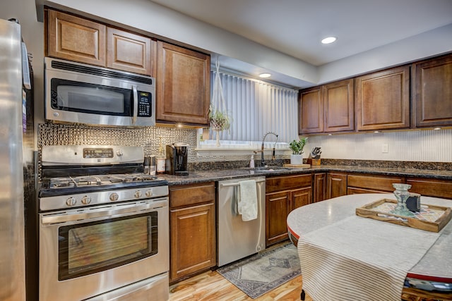 kitchen with light hardwood / wood-style floors, appliances with stainless steel finishes, backsplash, dark stone counters, and sink