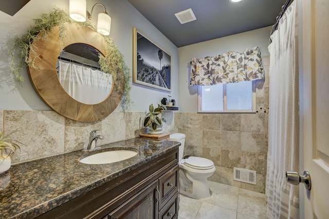 bathroom with toilet, tile patterned flooring, tile walls, and vanity