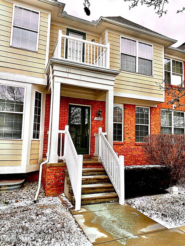 snow covered property entrance with a balcony and brick siding