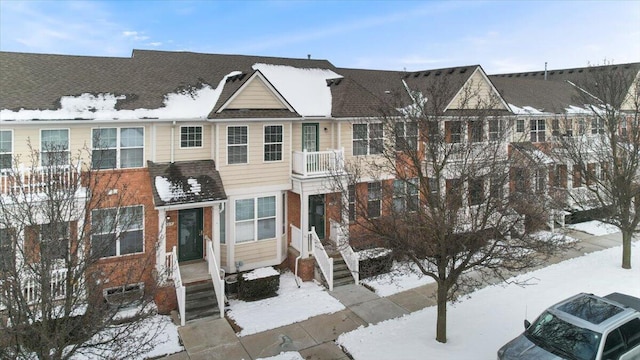 snow covered property with roof with shingles and brick siding