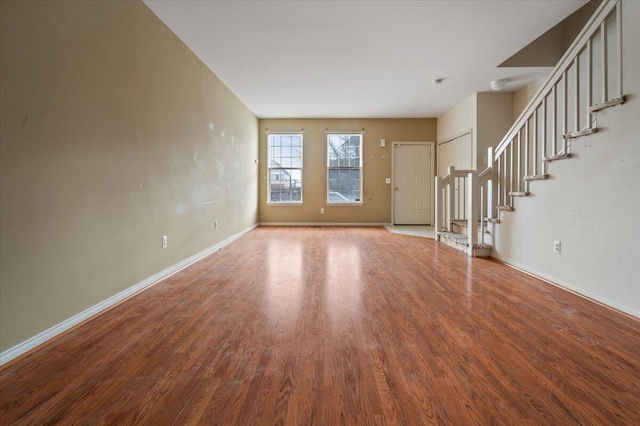 unfurnished living room with stairway, baseboards, and wood finished floors