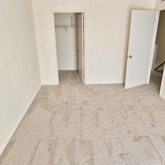 unfurnished bedroom featuring light carpet, a spacious closet, baseboards, and a closet