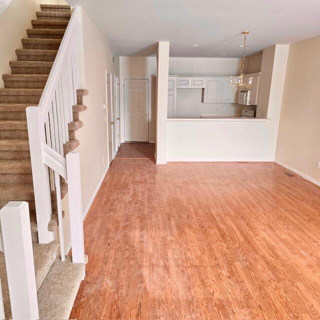 unfurnished living room featuring light wood-style floors, stairway, and baseboards