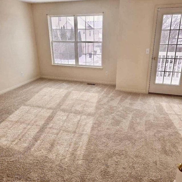 empty room featuring a healthy amount of sunlight, baseboards, and light colored carpet