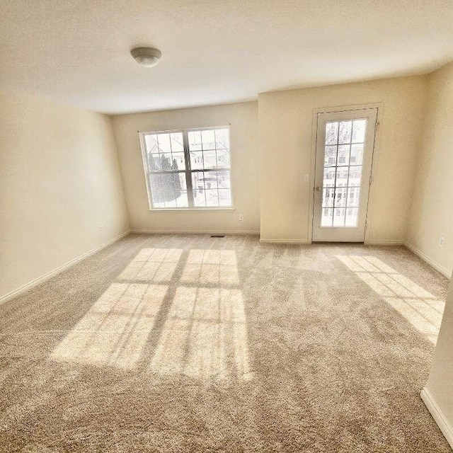 spare room with a healthy amount of sunlight, baseboards, a textured ceiling, and light colored carpet