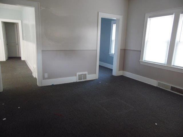 unfurnished room featuring dark carpet and a healthy amount of sunlight