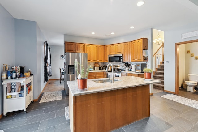 kitchen with sink, a center island with sink, stainless steel appliances, and tasteful backsplash