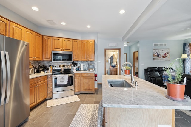 kitchen with sink, stainless steel appliances, backsplash, and an island with sink