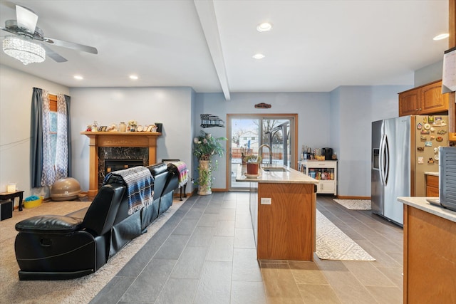 kitchen with beamed ceiling, a fireplace, stainless steel fridge with ice dispenser, a kitchen island with sink, and sink