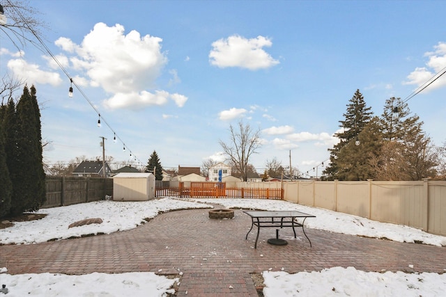 yard covered in snow featuring a patio area, a fire pit, and a storage unit