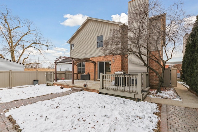 snow covered back of property featuring a deck and a pergola