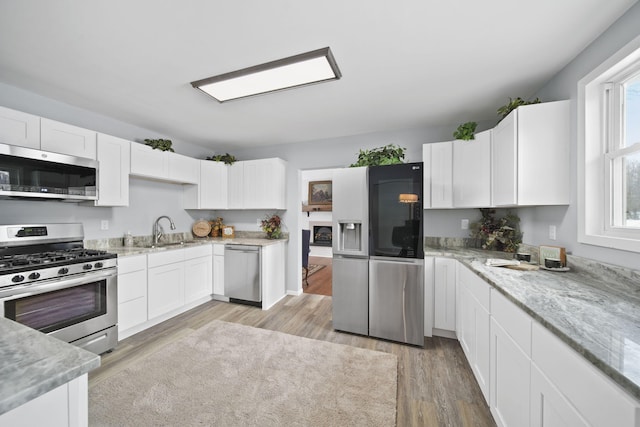 kitchen with light wood-type flooring, light stone countertops, stainless steel appliances, and white cabinetry