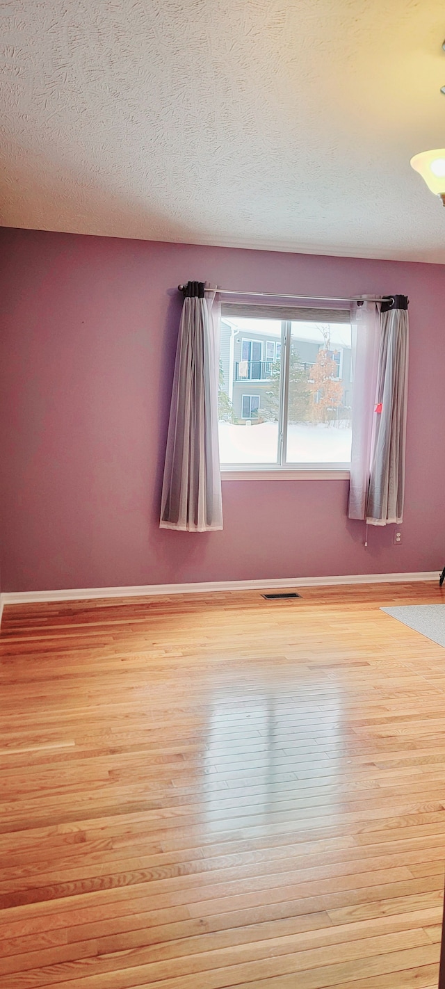 spare room with a textured ceiling and light hardwood / wood-style flooring